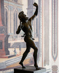 A bronze statue of a nude male figure in a dynamic pose, mounted on a dark pedestal in front of a large classical architectural mural.